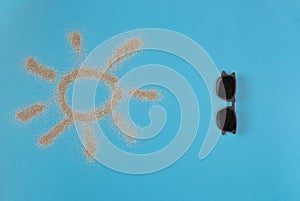 Sun drawn by the sand on blue background. Sunglasses isolated on blue background