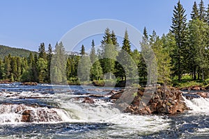 A sun-drenched summer view of the Namsen River in Namsskogan, Trondelag, Norway, featuring cascades