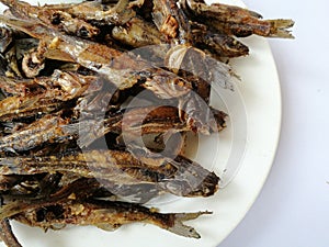 Sun dried fish and salty. small fish fried on white dish. top view and background.