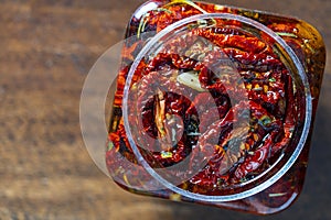 Sun-dried red tomatoes with garlic, green rosemary, olive oil and spices in a glass jar on a wooden table. Rustic style, top view