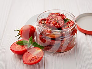 Sun-dried tomatoes dressed with olive oil and spices in a glass jar on a white wooden background