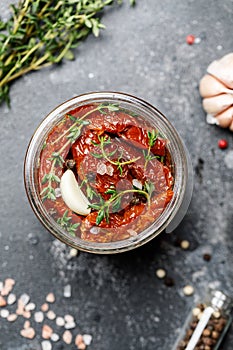 Sun dried tomatoes with fresh herbs and spices, sea salt in olive oil in a glass jar. Top view. Print for kitchen