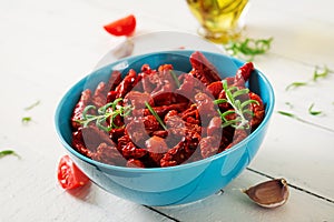 Sun dried tomatoes with herbs and garlic in bowl on wooden table.