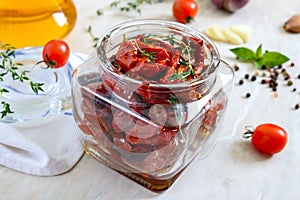 Sun-dried tomatoes with herbs, garlic in olive oil in a glass jar on a light background