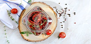 Sun-dried tomatoes with herbs, garlic in olive oil in a glass jar on a light background. Top view, flat lay