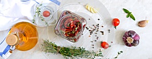 Sun-dried tomatoes with herbs, garlic in olive oil in a glass jar on a light background. Top view, flat lay. Banner