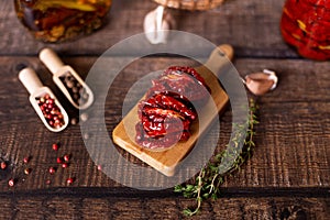 Sun-dried tomatoes in olive oil on a mini board with pepper, garlic and thyme in a rustic style. Selective focus, close-up