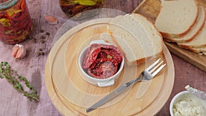 Sun-dried tomatoes in olive oil in a white bowl with homemade bread and cottage cheese on a wooden board. Home cooking, rustic.