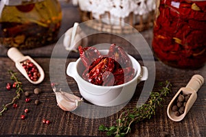 Sun-dried tomatoes in olive oil in a white bowl with pepper, garlic and thyme in a rustic style. Selective focus, close-up