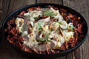 Sun-dried tomatoes with pasta, parsley in an iron black pan on a natural wooden background. Close up