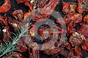 Sun-dried tomatoes with spices and garlic on a baking sheet. On top of them lies fresh rosemary