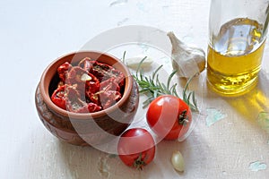 Sun-dried tomatoes with spices and garlic in a clay pot. Nearby is a bottle with olive oil, tomatoes, rosemary and garlic