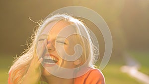 SUN FLARE: Blonde haired woman laughing while lying in the middle of a meadow.