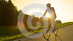 SUN FLARE: Golden sun rays illuminate athletic man pedaling his road bicycle.