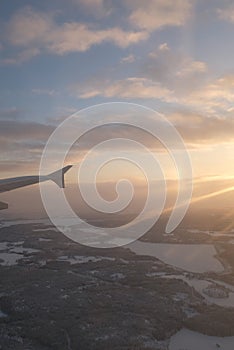 Sun flare shining on a window airplane wing over a winter white landscape over Helsinki, Finland in a winter sunset landscape