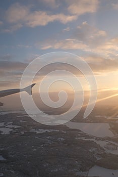 Sun flare shining on a window airplane wing over a winter white landscape over Helsinki, Finland in a winter sunset landscape