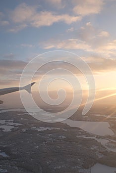 Sun flare shining on a window airplane wing over a winter white landscape over Helsinki, Finland in a winter sunset landscape