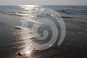 Sun glare on the waves of the North Sea at sunset. Footprints in the wet sand and evening sky. Ostend, Belgium