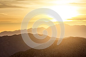 Sun glowing behind clouds and mountains in a desert landscape sc