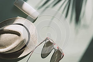 Sun hat, glasses and spf cream or lotion unbranded package on light blue background with palm tree leaf shadow, top view