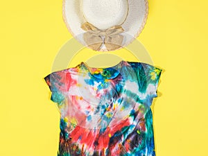 A sun hat and tie dye t-shirt on a yellow background. Flat lay.