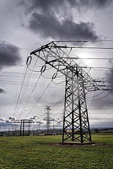 Sun hidden behind dramatic clouds and electricity pylons conducting current from distribution power station