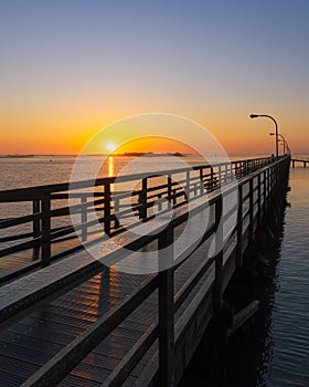 Sun on the horizon illuminating a wooden boardwalk fishing pier with golden light