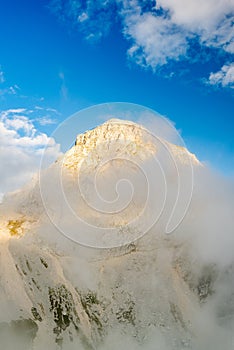 Sun Illuminated Mangart Mountains Peak in Clouds and Fog