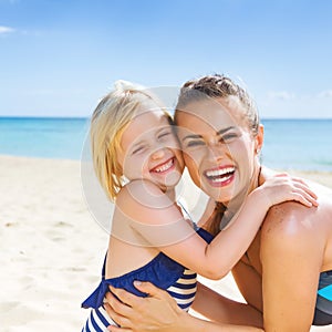Smiling healthy mother and daughter on seashore embracing
