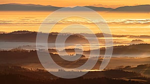 Sun light rays during sunshine peaking through morning mist on a wavy landscape with a church on top of a hill