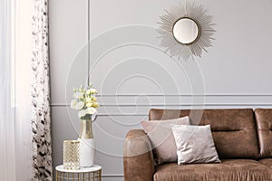 Sun like shaped mirror above leather sofa with pillows in grey elegant living room