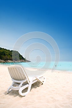 Sun lounger on sandy beach against blue sky