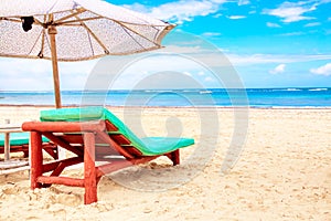 A sun lounger under an umbrella on the sandy beach by the ocean and cloudy sky. Vacation background. Idyllic beach landscape