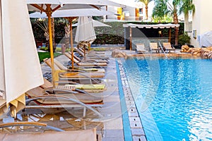 Sun loungers and blue clear water in the swimming pool. Tropical resort