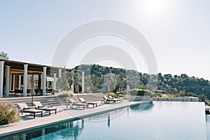 Sun loungers with folded sun umbrellas line the pillared terrace next to the long swimming pool. Hotel Amanzoe