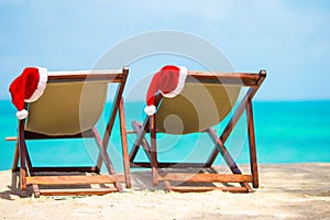 Sun loungers with Santa Hat at beautiful tropical beach with white sand and turquoise water. Perfect Christmas vacation