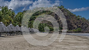 Sun loungers stand in a row on the sandy beach under straw umbrellas