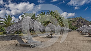 Sun loungers stand in rows under straw sun umbrellas on the sandy beach.