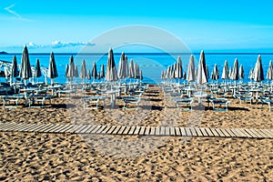 Sun loungers and umbrellas on public beach at summer sunny mornin. Skojl island background. Calm sea and blue sky Becici, photo