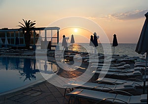 Sun lounges overlooking infinity pool and beach at sunset in a resort. Rhodes