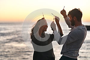 The sun may go down but love always burns bright. a happy young couple having fun with sparklers on the beach at sunset.