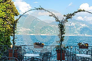 Sun on mountain side across Lake Como through vines over arches on lake edge Menaggio, Italy