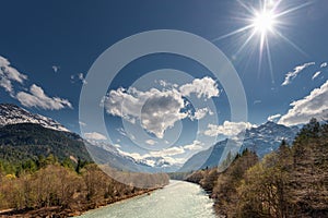 Sun over rural river between mountains