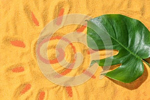 A sun painted on the sand and a green leaf