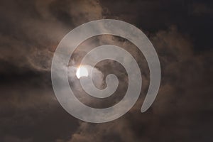 The sun during a partial solar eclipse with dark clouds .