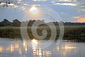 SUN PARTIALLY HIDDEN BEHIND CLOUDS REFLECTING ON WATER AT SUNDOWN