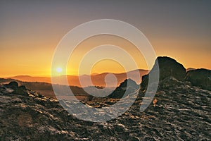 Sun peaking over the mountains in germany beside a large rock formation