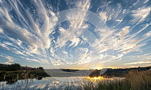 The sun peeking through a fluffy cumulus clouds, clouds reflected in water surface, sunset on the lake