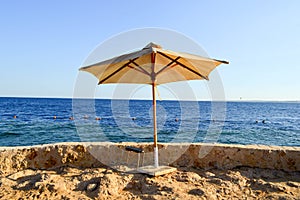 Sun-protecting beautiful umbrellas made of yellow fabric against the blue sky, on the shore of the salt sea with stone handrails a