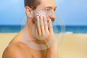 Sun protection. Man applying sunblock onto face on beach, closeup